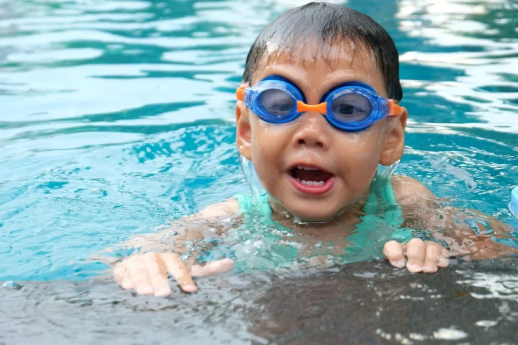 A toddler swimming on a pool wearing blue goggles